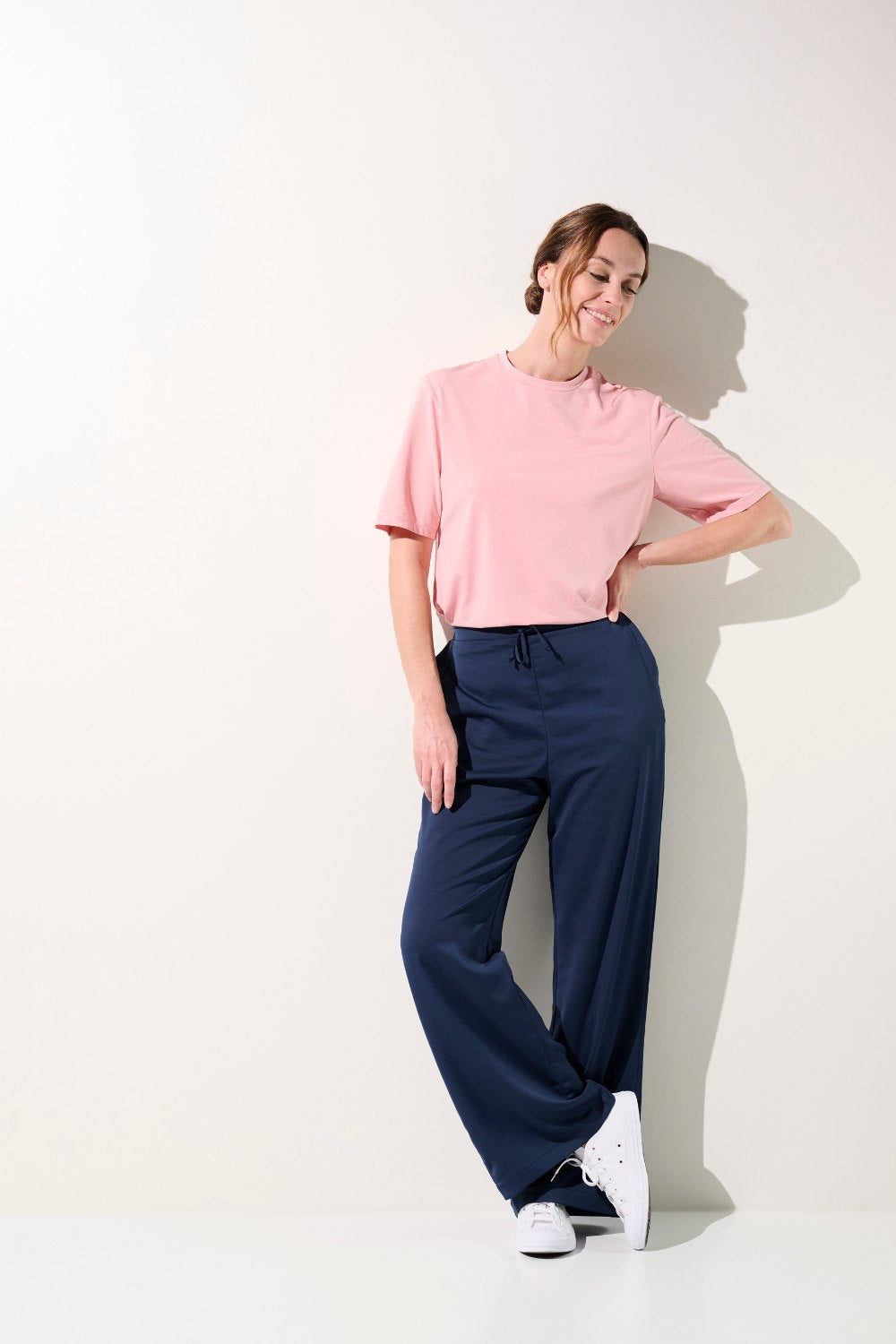 Femme en t-shirt anti-UV rose, confortable et élégant, associé à un pantalon ample pour un look décontracté.