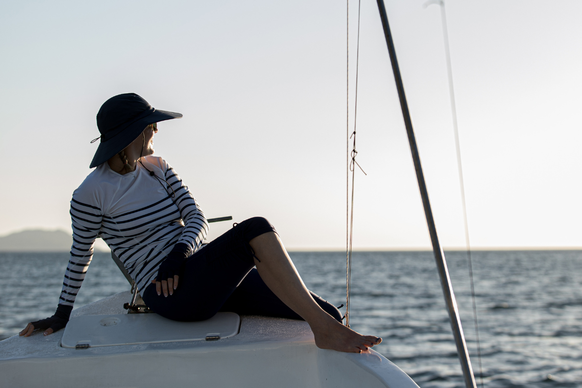 Femme portant des vêtements anti-UV et un chapeau UPF 50+ sur un voilier, regardant au large.